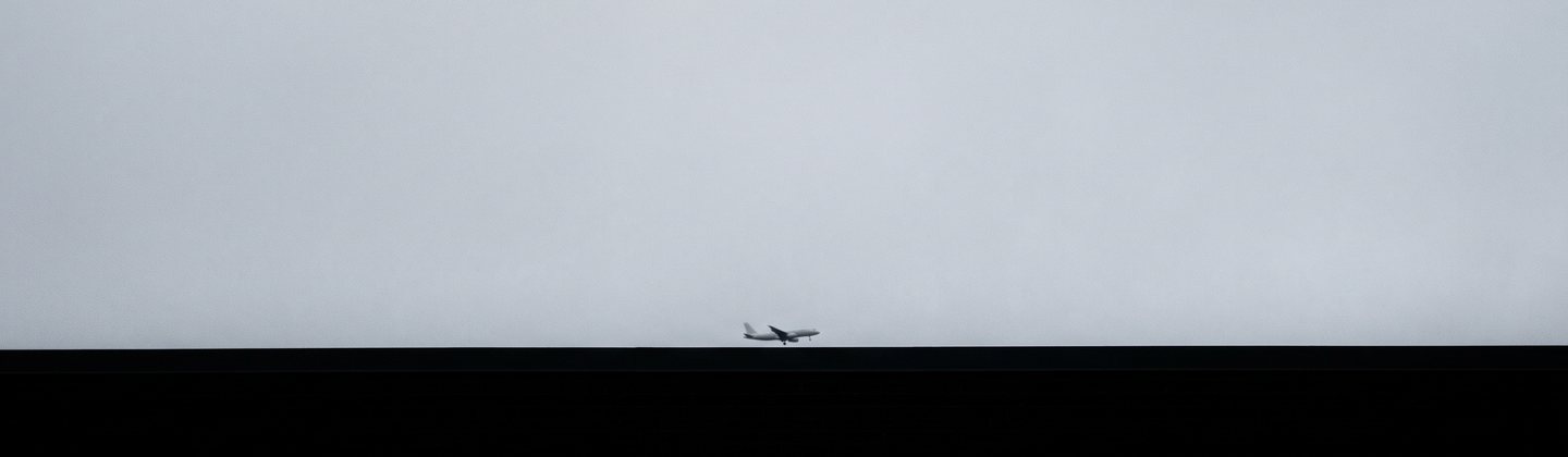 Силуэт самолёта высоко в небе над тёмной линией крыши